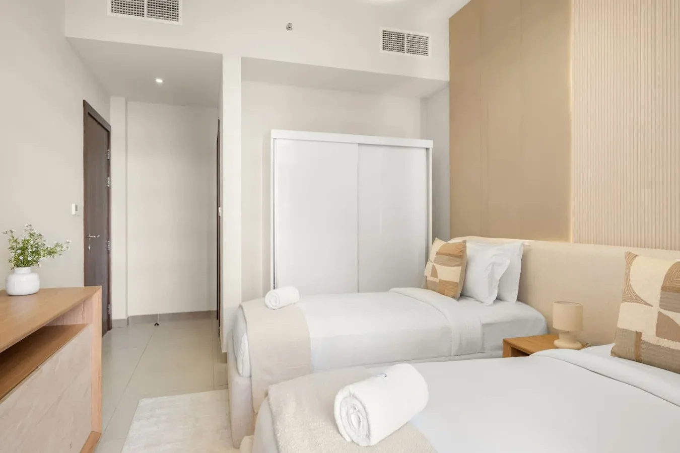Un dormitorio luminoso con dos camas, ropa de cama blanca y una mesita de noche.