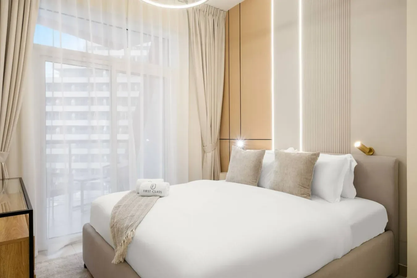 Un dormitorio luminoso con una cama tendida junto a una gran ventana con cortinas.