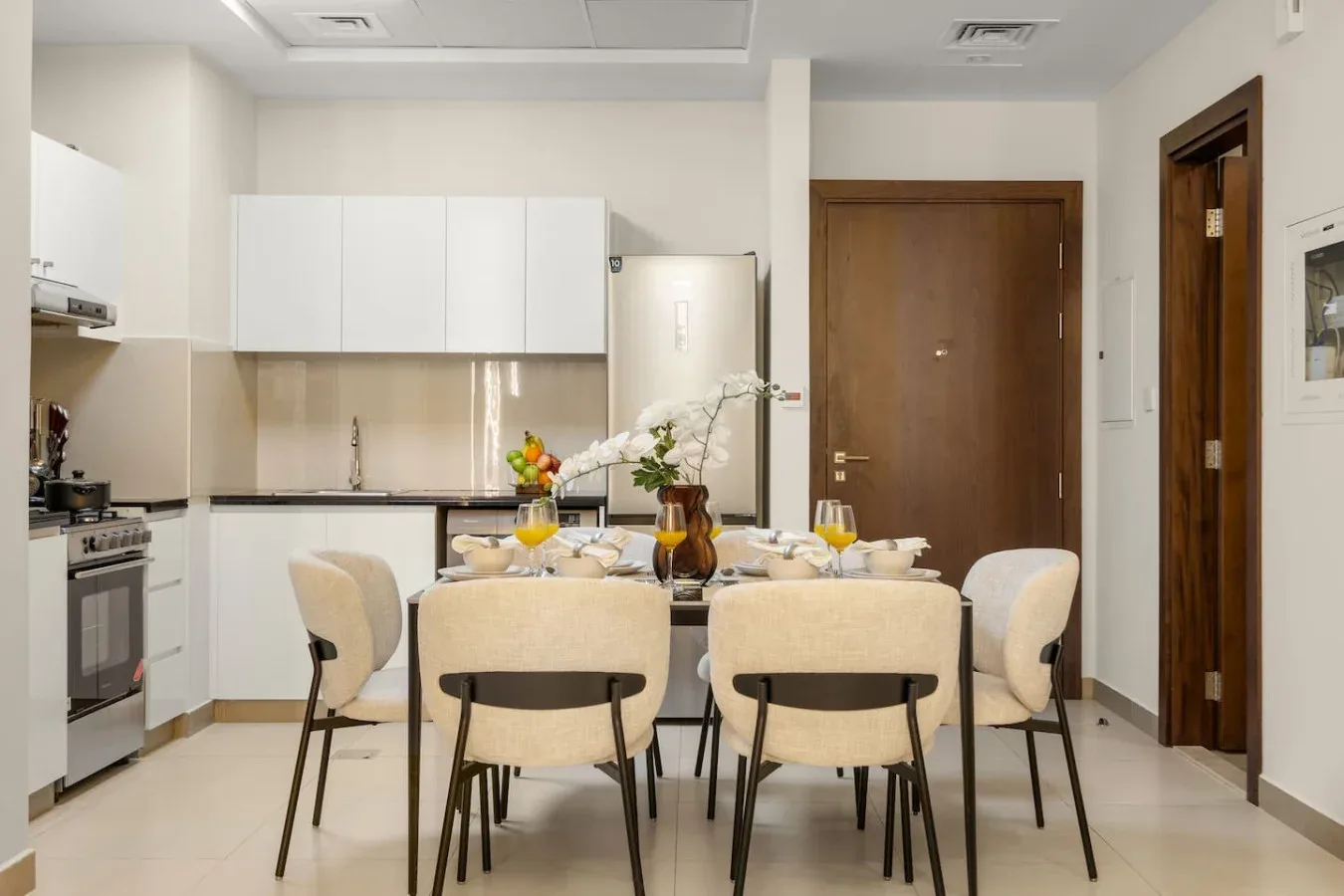 Un comedor con mesa y asientos tapizados está junto a una cocina compacta.