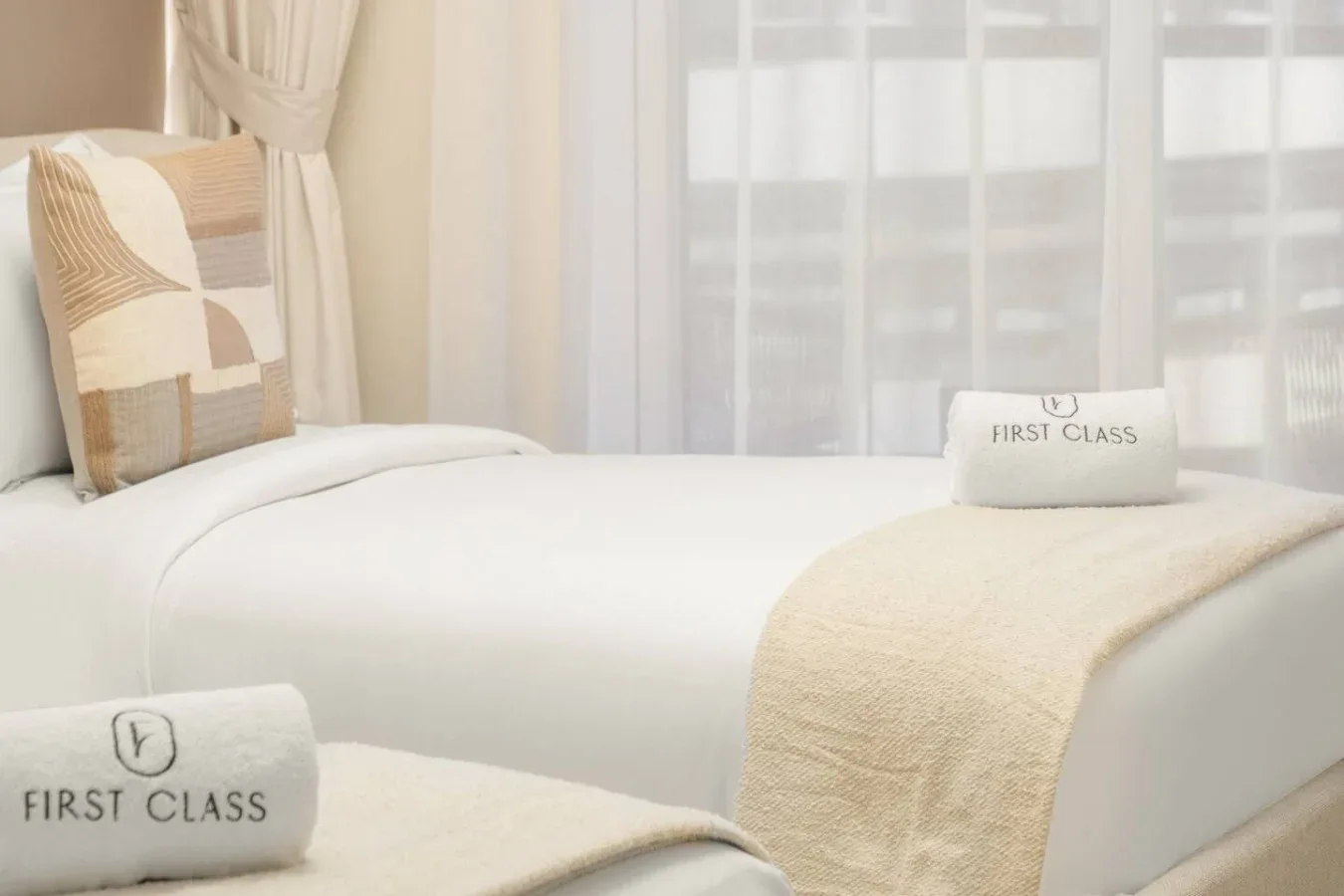 Un dormitorio con ropa de cama blanca y cortinas translúcidas en la ventana.