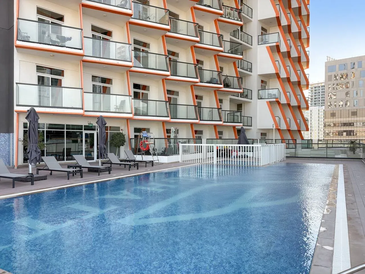Una piscina al aire libre está junto a un edificio moderno con balcones.