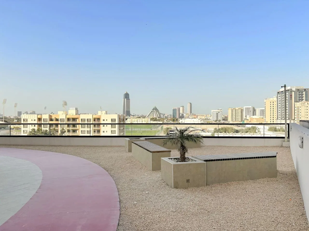 Una terraza en la azotea da a un horizonte urbano, con un camino curvo rosa y jardineras.