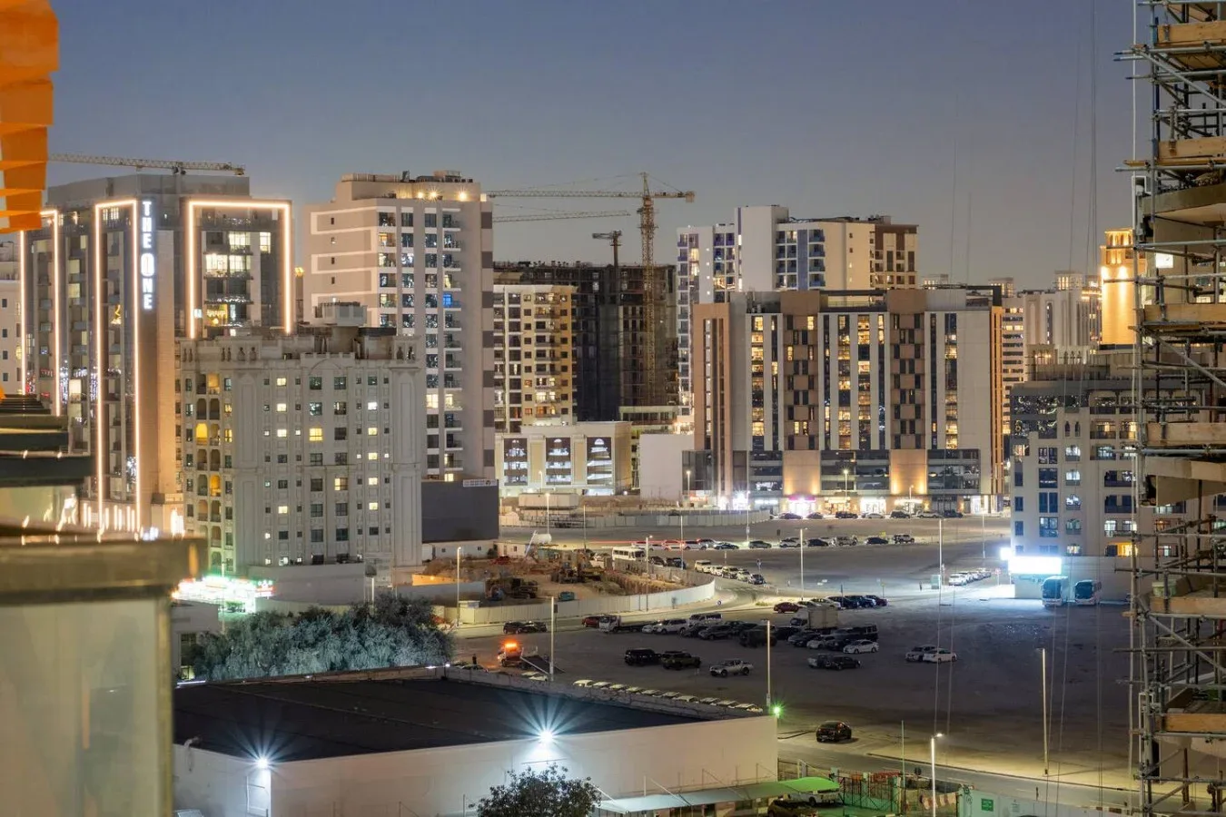 Un paisaje urbano nocturno muestra edificios iluminados y una obra en construcción.