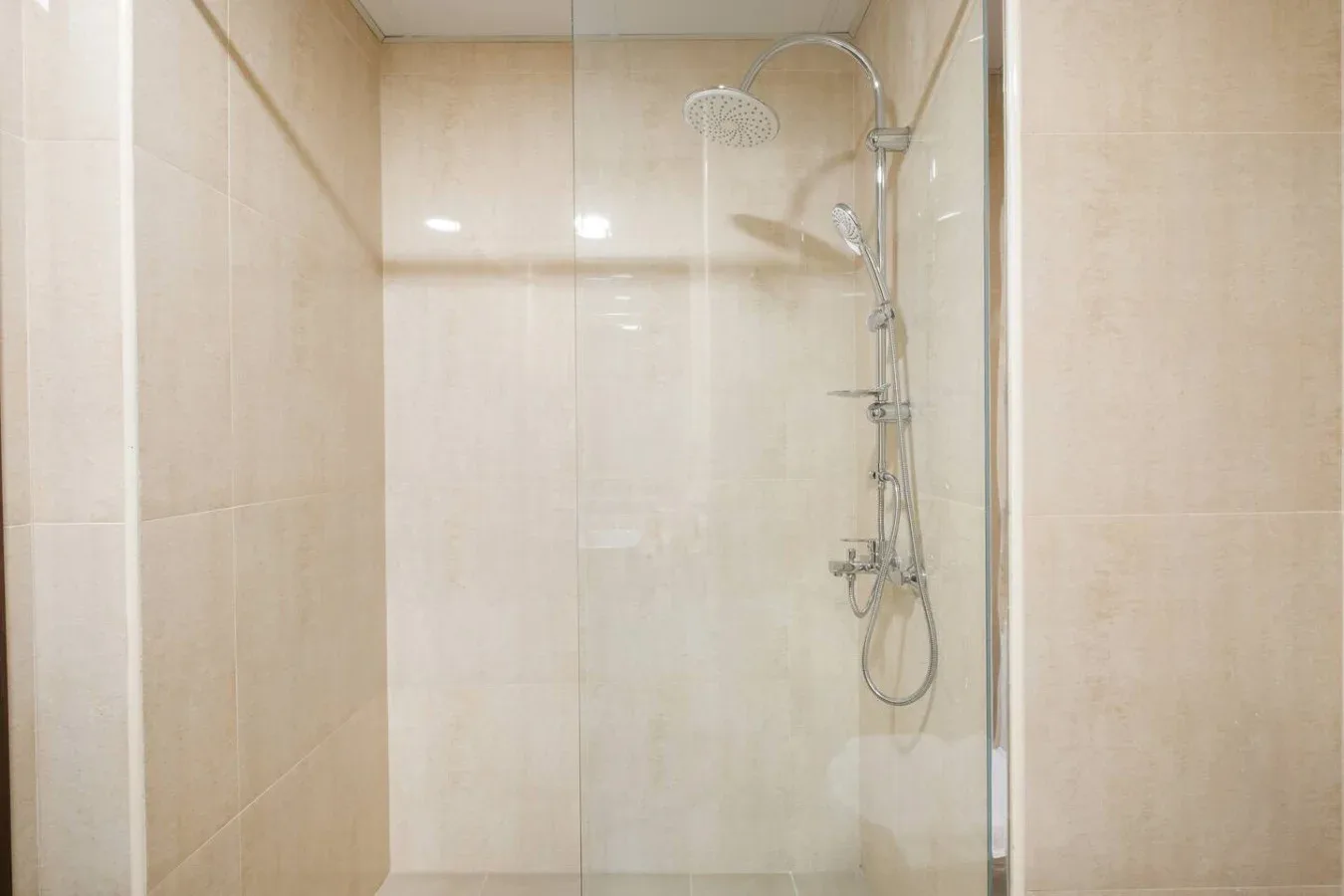 Una ducha revestida de azulejos, con un panel de vidrio y accesorios montados en la pared.