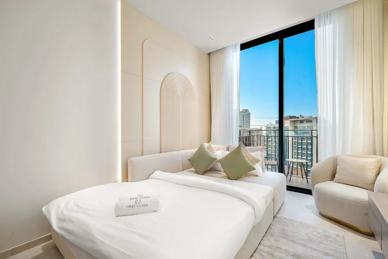 Un dormitorio luminoso con una cama tendida junto a grandes ventanas con vistas a la ciudad.