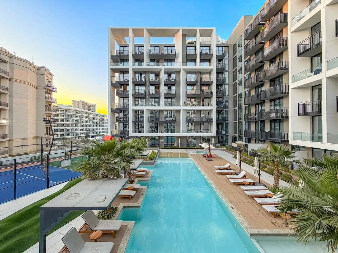 Una piscina en un patio entre edificios modernos, con asientos para descansar y vegetación.
