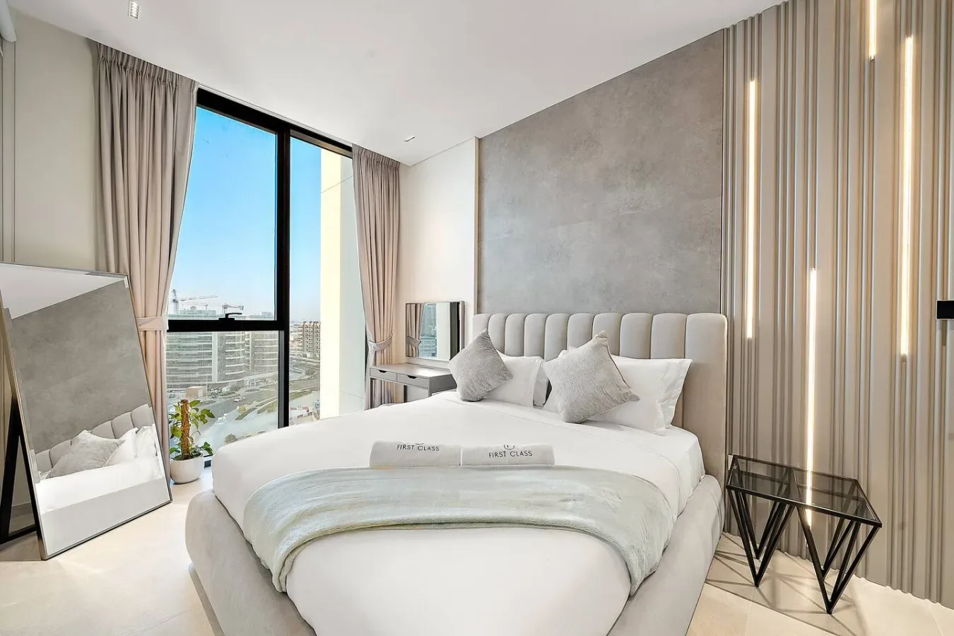 Un dormitorio luminoso con una cama bien tendida junto a ventanas altas.