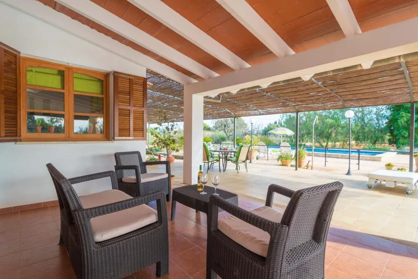 Un patio cubierto con asientos acolchados da a un jardín y una piscina.