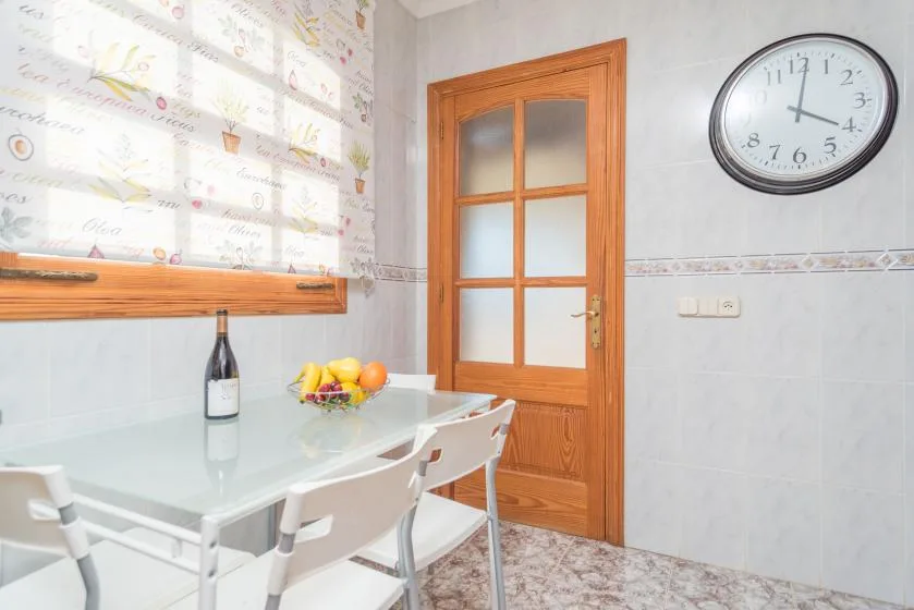 Un comedor con una mesa de vidrio, asientos blancos y una puerta de madera.