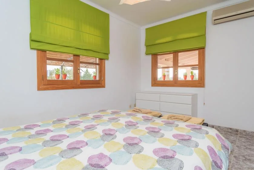 Un dormitorio con una cama bajo dos ventanas con persianas verdes.