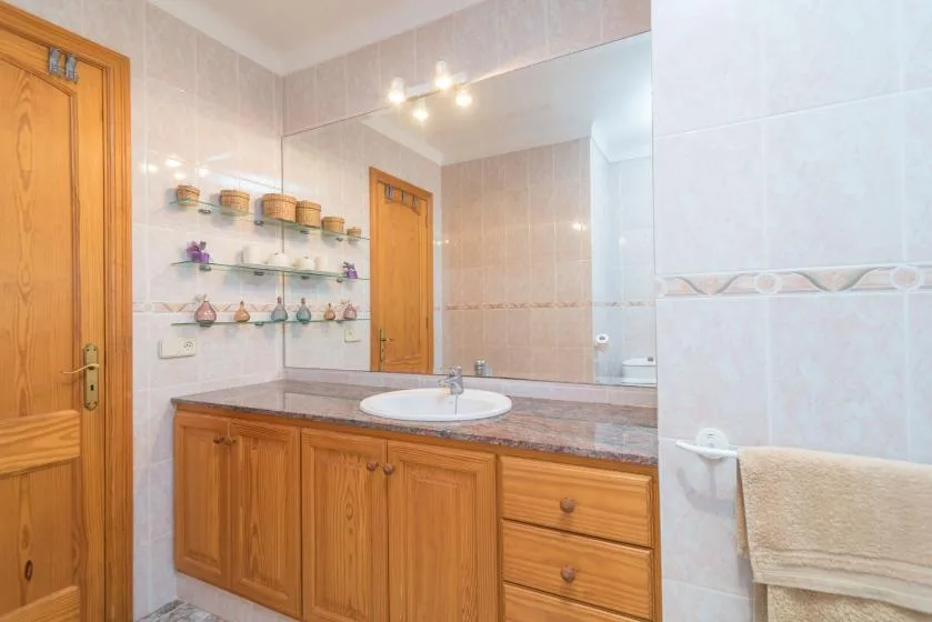 Un baño alicatado con mueble de madera, lavabo y espejo.
