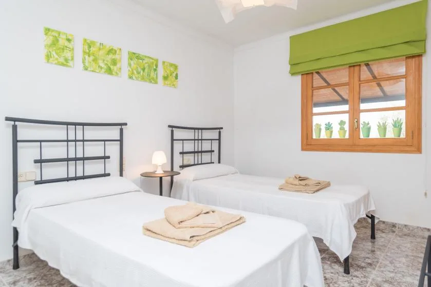 Un dormitorio luminoso con dos camas y una ventana con vistas a la vegetación.