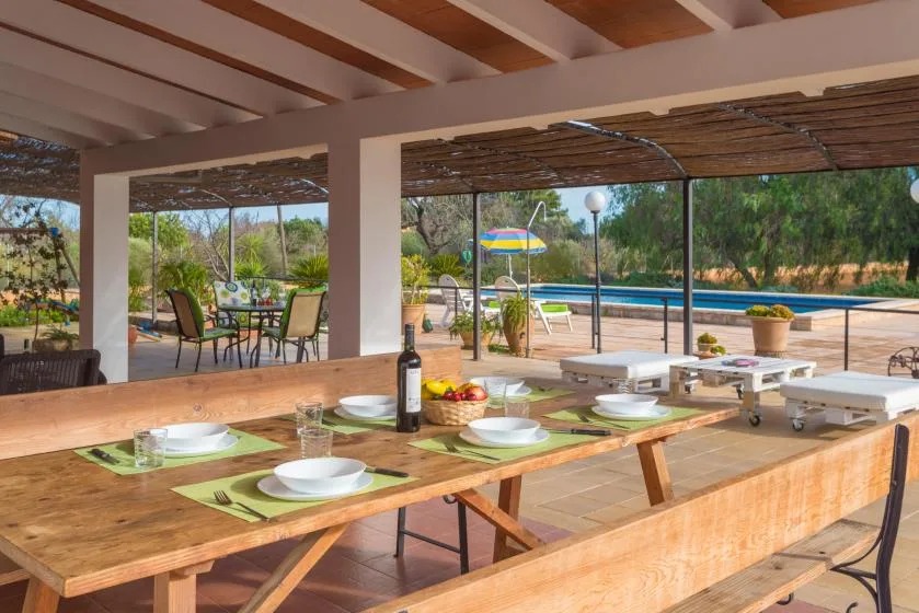 Una zona de comedor exterior cubierta da a una piscina y un jardín ajardinado.