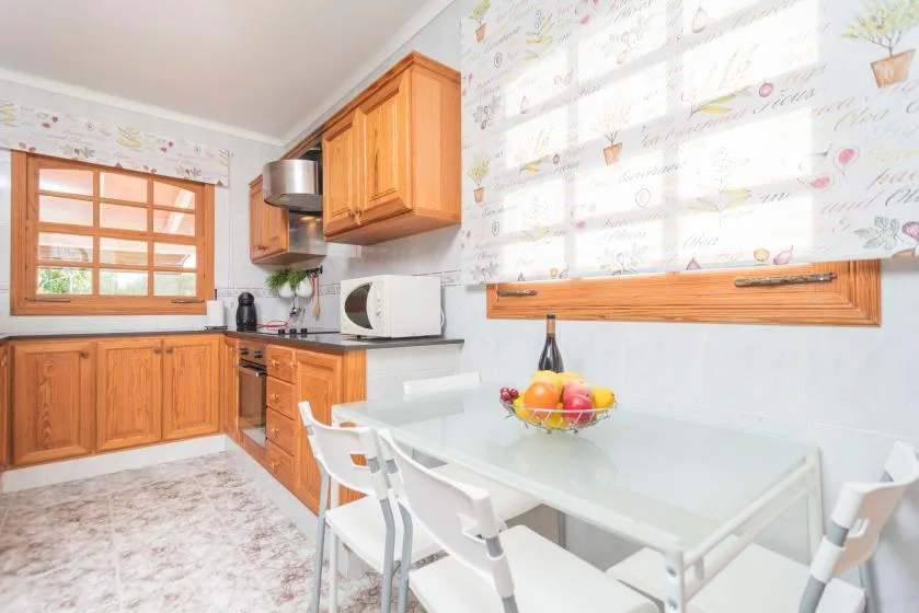 Una cocina luminosa con zona de comedor, armarios de madera y una mesa de cristal.