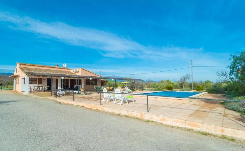 Una casa baja está junto a una piscina al aire libre y un patio pavimentado.