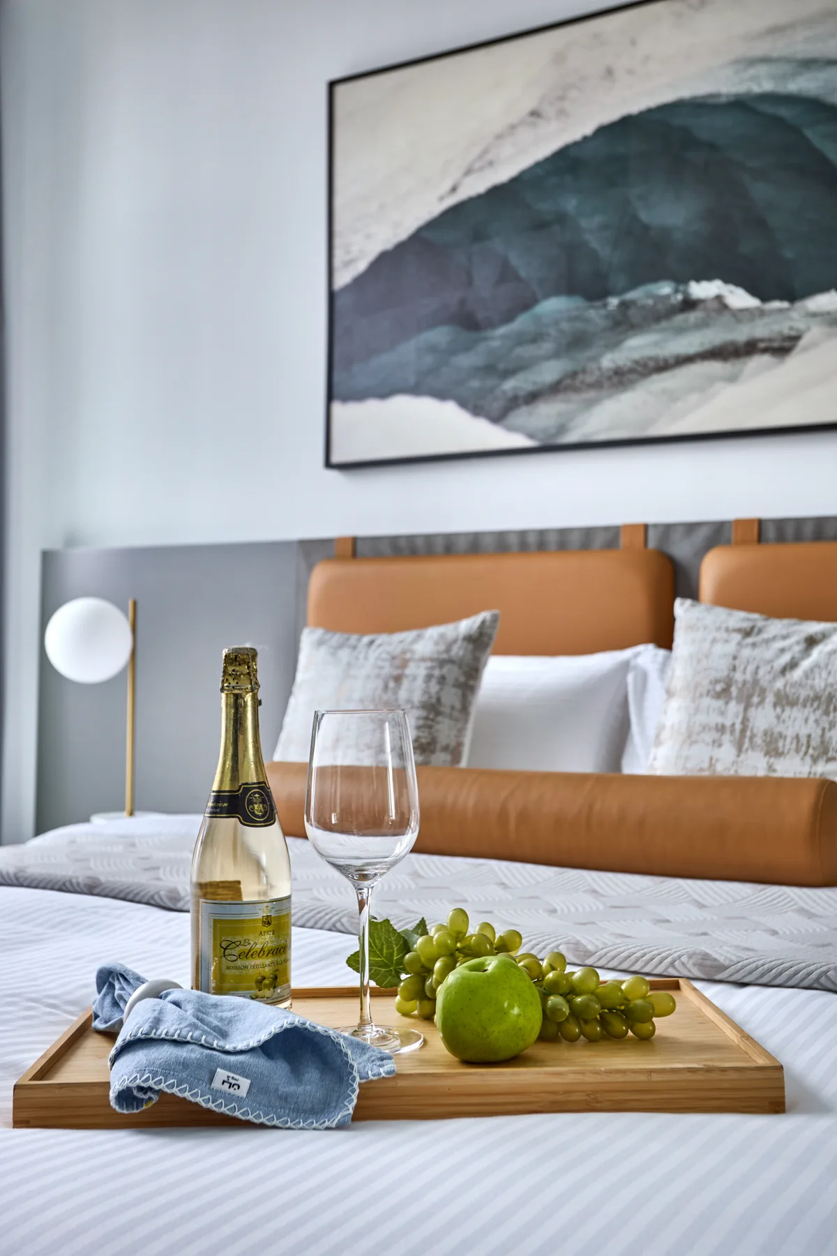 Un dormitorio con una cama tendida, fruta y una copa de vino sobre una bandeja.