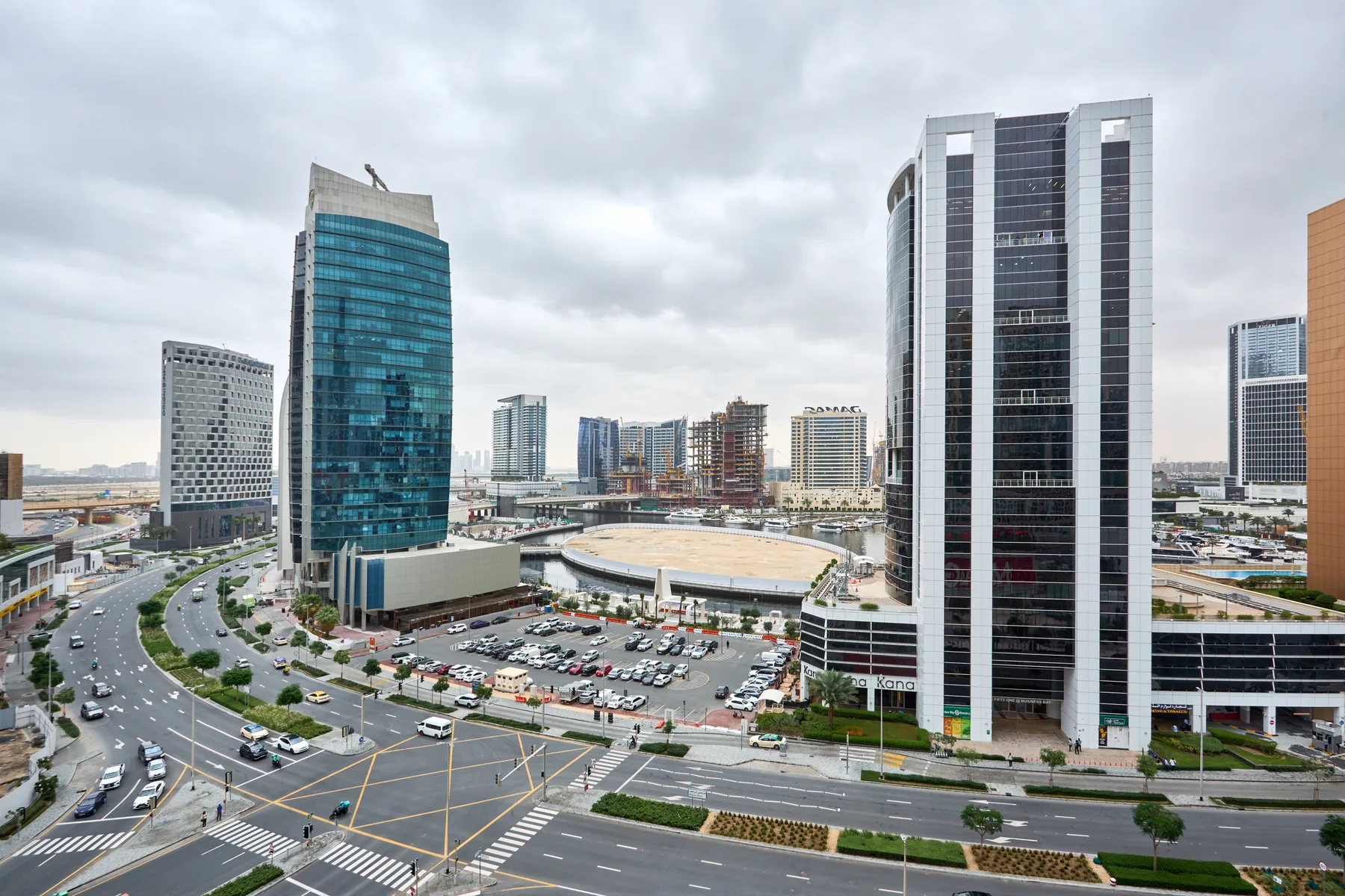 Un paisaje urbano con torres de oficinas modernas, calles y medianas ajardinadas bajo un cielo nublado.