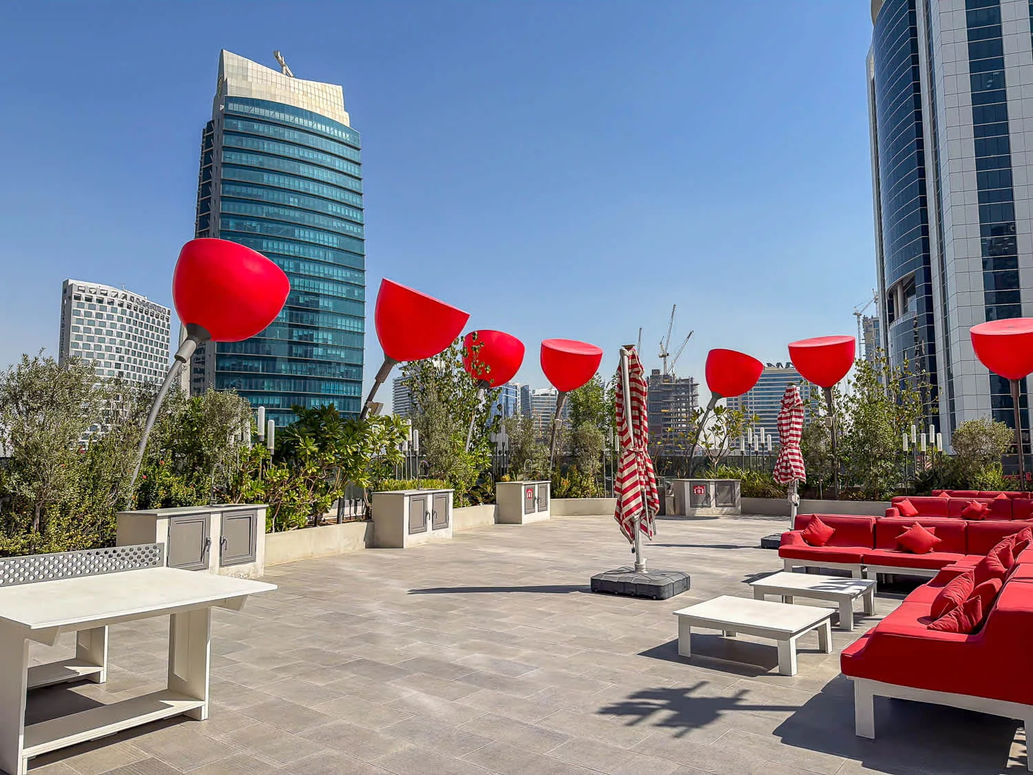 Una terraza en la azotea tiene asientos rojos, mesas y grandes lámparas escultóricas rojas.