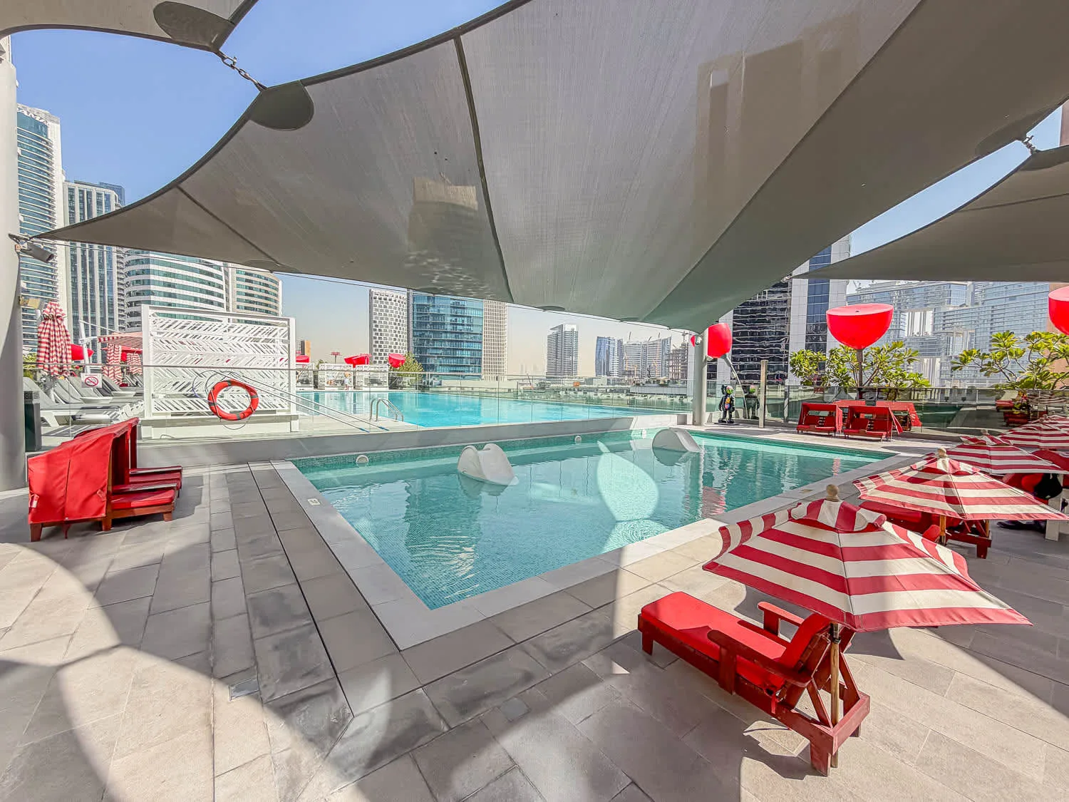 Una piscina en la azotea está bajo grandes toldos, con edificios de la ciudad al fondo.