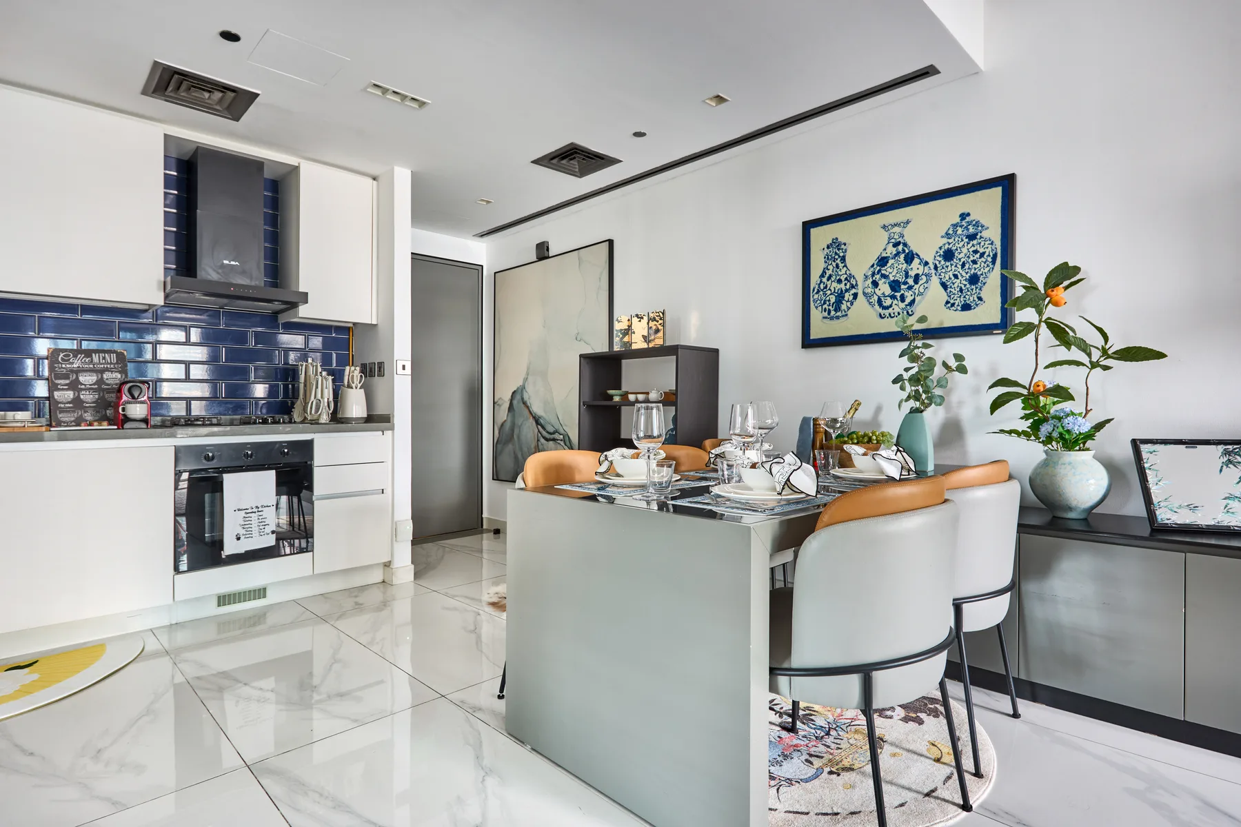 Un comedor luminoso con una mesa puesta, armarios blancos y un salpicadero de azulejos azules.