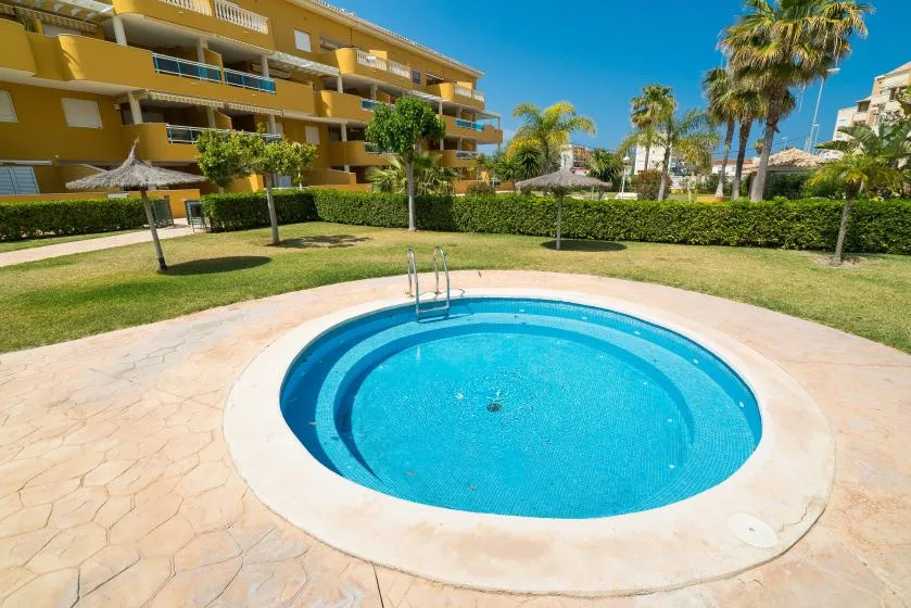 Una piscina circular está en un patio ajardinado junto a un edificio de apartamentos.