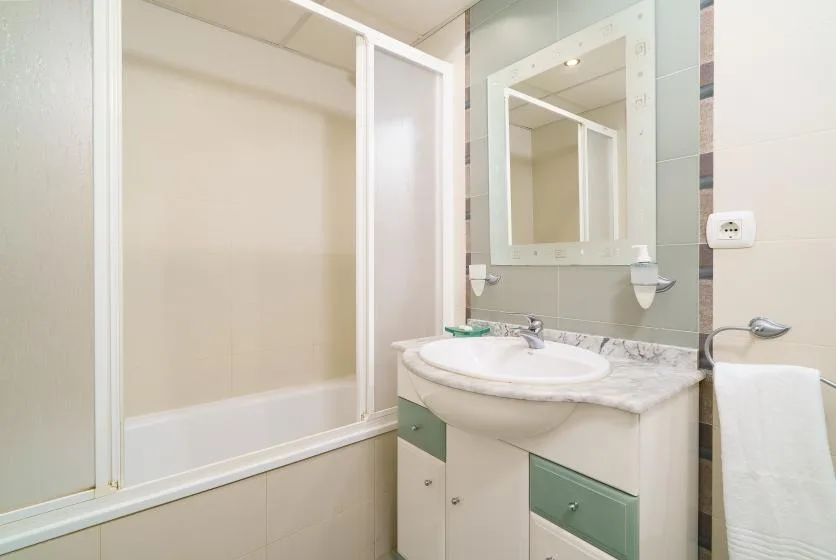 Un baño con bañera, mampara de vidrio y lavabo bajo un espejo.