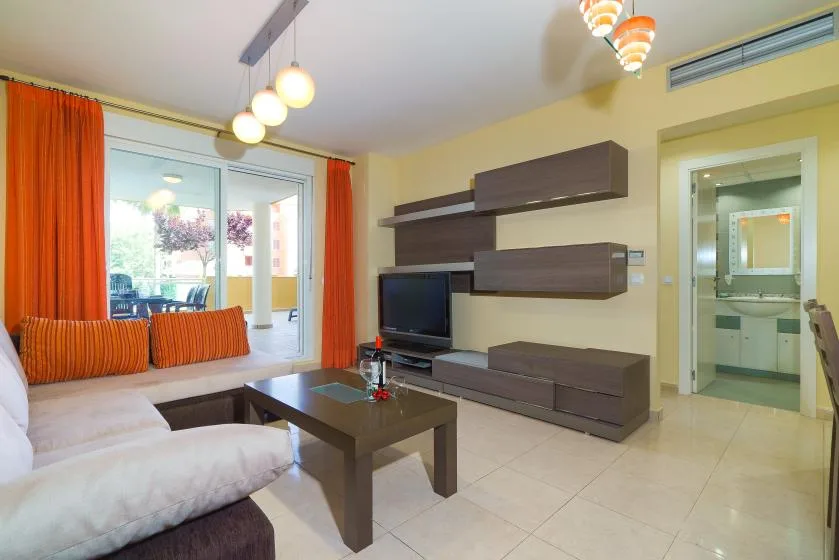 Una sala de estar con asientos, un televisor y una puerta de vidrio que da a un balcón.