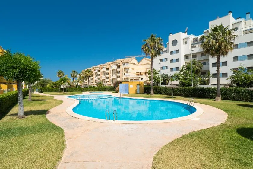 Una piscina está rodeada de jardines y edificios de apartamentos bajo un cielo azul despejado.