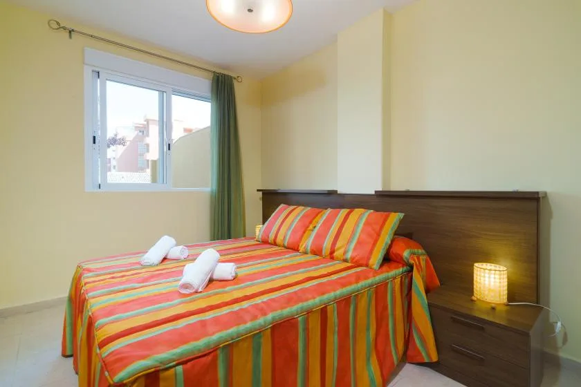 Un dormitorio con una colcha de rayas coloridas y una ventana con cortinas.