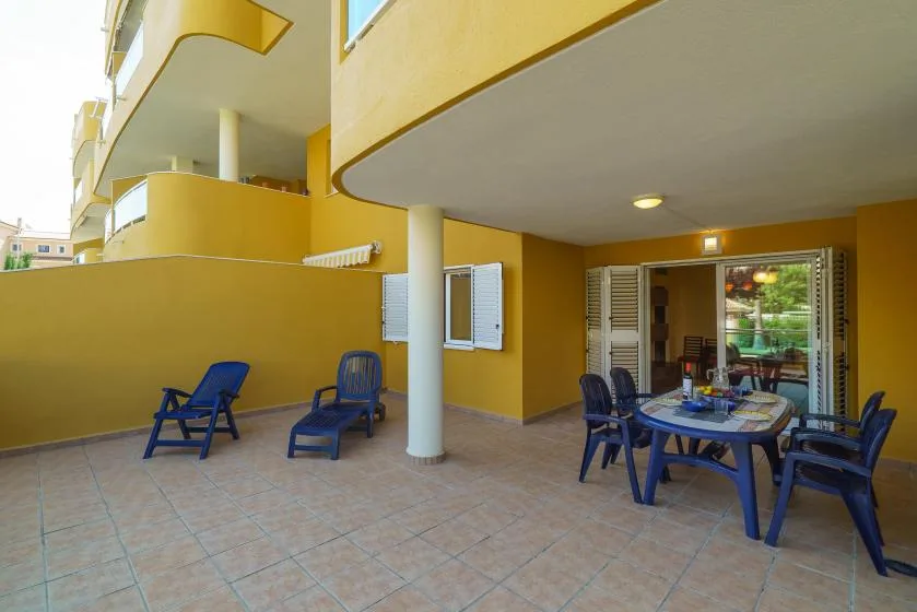 Un patio exterior con suelo de baldosas, asientos azules y una mesa junto a una puerta abierta.