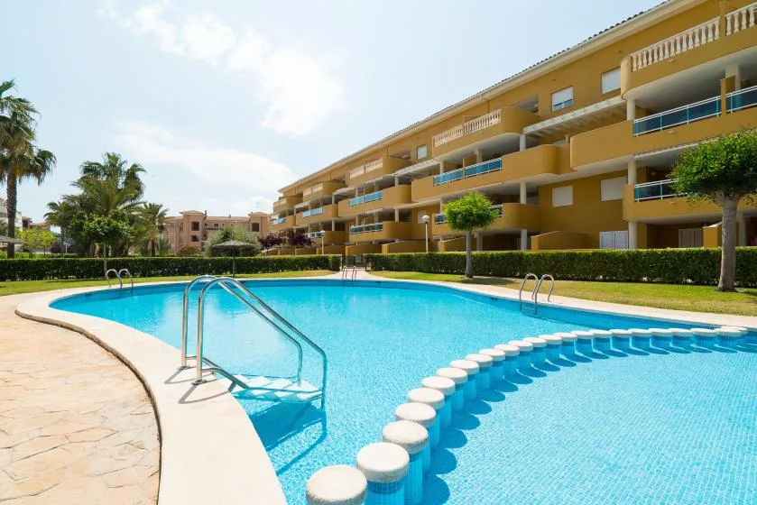 Una piscina junto a un edificio amarillo de varias plantas, con piedras curvas que atraviesan el agua.
