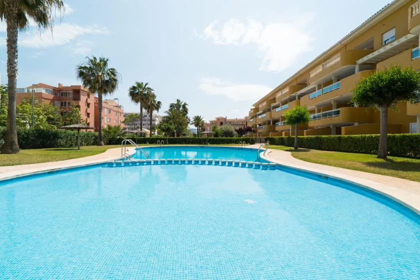 Una piscina exterior luminosa está junto a edificios de apartamentos y palmeras.