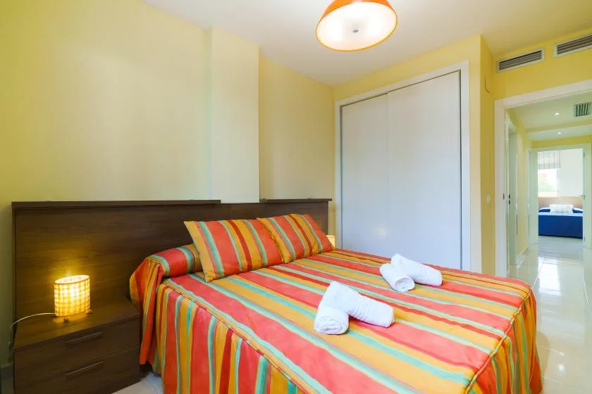 Un dormitorio con una cama cubierta con ropa de cama a rayas de colores junto a un cabecero oscuro.
