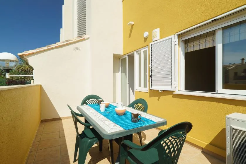 Una zona de comedor exterior soleada tiene una mesa con mantel turquesa y asientos verdes.