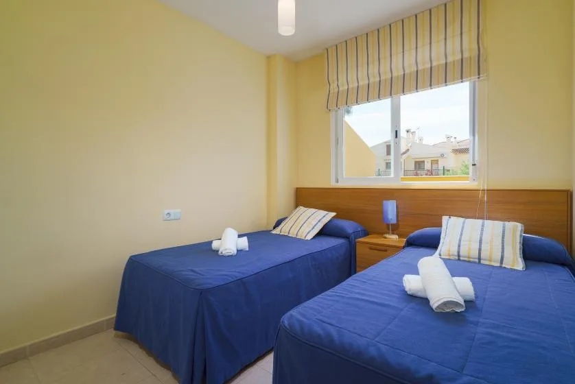 Un dormitorio con dos camas azules y una ventana con cortinas a rayas.