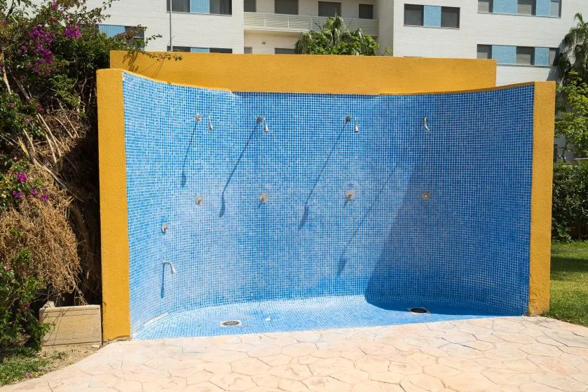 Una pared exterior de ducha revestida de azulejos está junto a un patio pavimentado.
