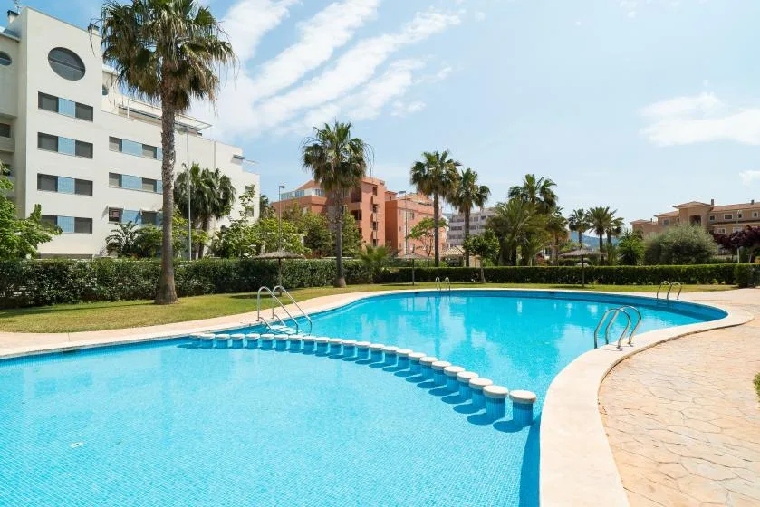 Una piscina exterior ajardinada está rodeada de palmeras y edificios de apartamentos.