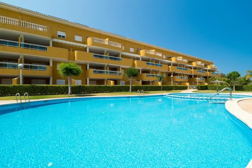 Una gran piscina al aire libre está frente a una fila de edificios de apartamentos amarillos.