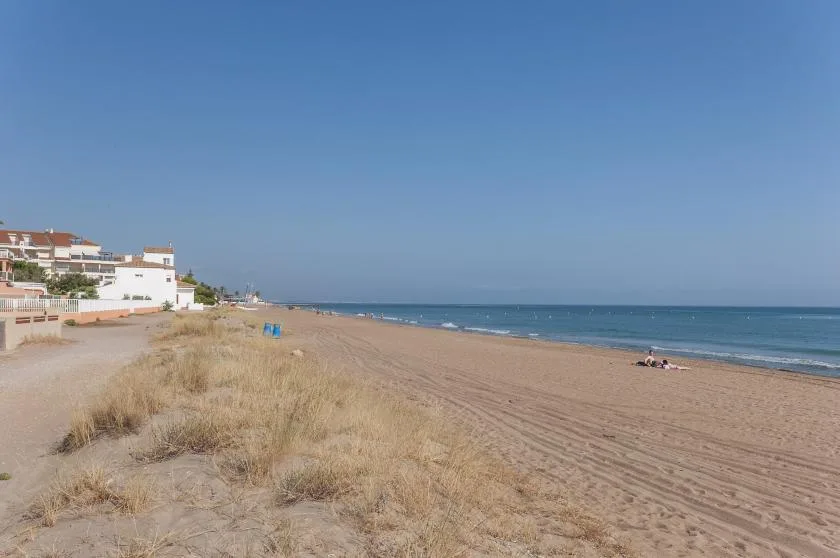 Una playa de arena se extiende junto al mar, con edificios en la orilla.