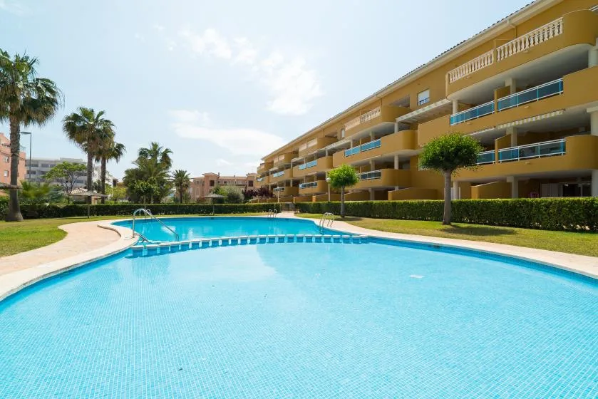Una piscina está junto a un patio ajardinado y un edificio de varias plantas.