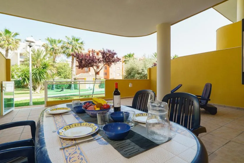 Comedor exterior cubierto con la mesa puesta y vistas a un patio ajardinado.