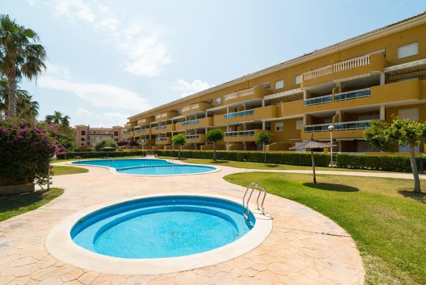 Una piscina y una piscina infantil circular están junto a un edificio de apartamentos ajardinado.