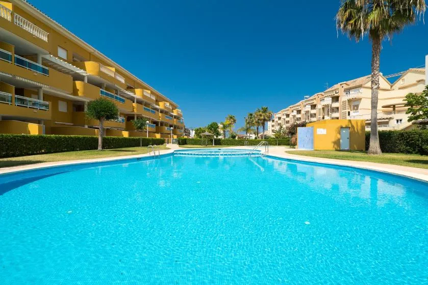 Una piscina se encuentra entre hileras de edificios de apartamentos bajo un cielo azul despejado.
