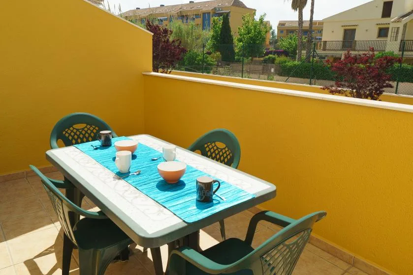 Una zona de comedor al aire libre con una mesa y sillas junto a una pared amarilla.