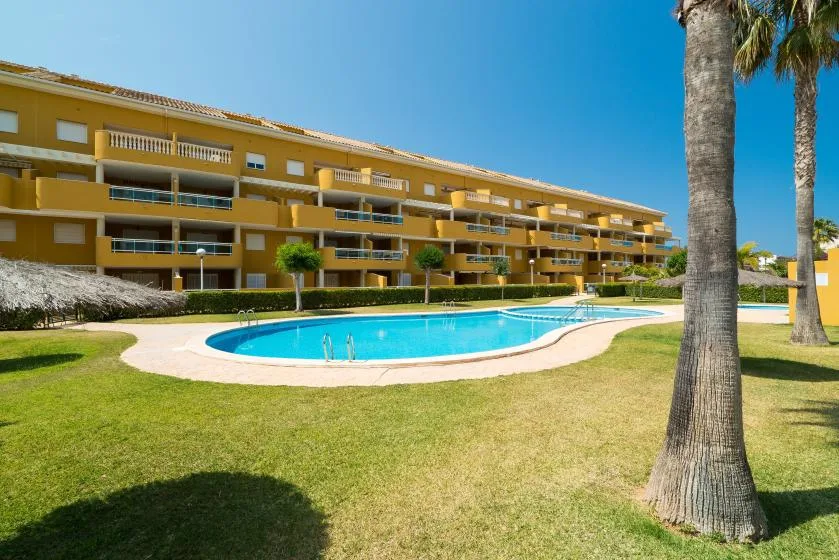 Una piscina está en un césped frente a un edificio amarillo de apartamentos.