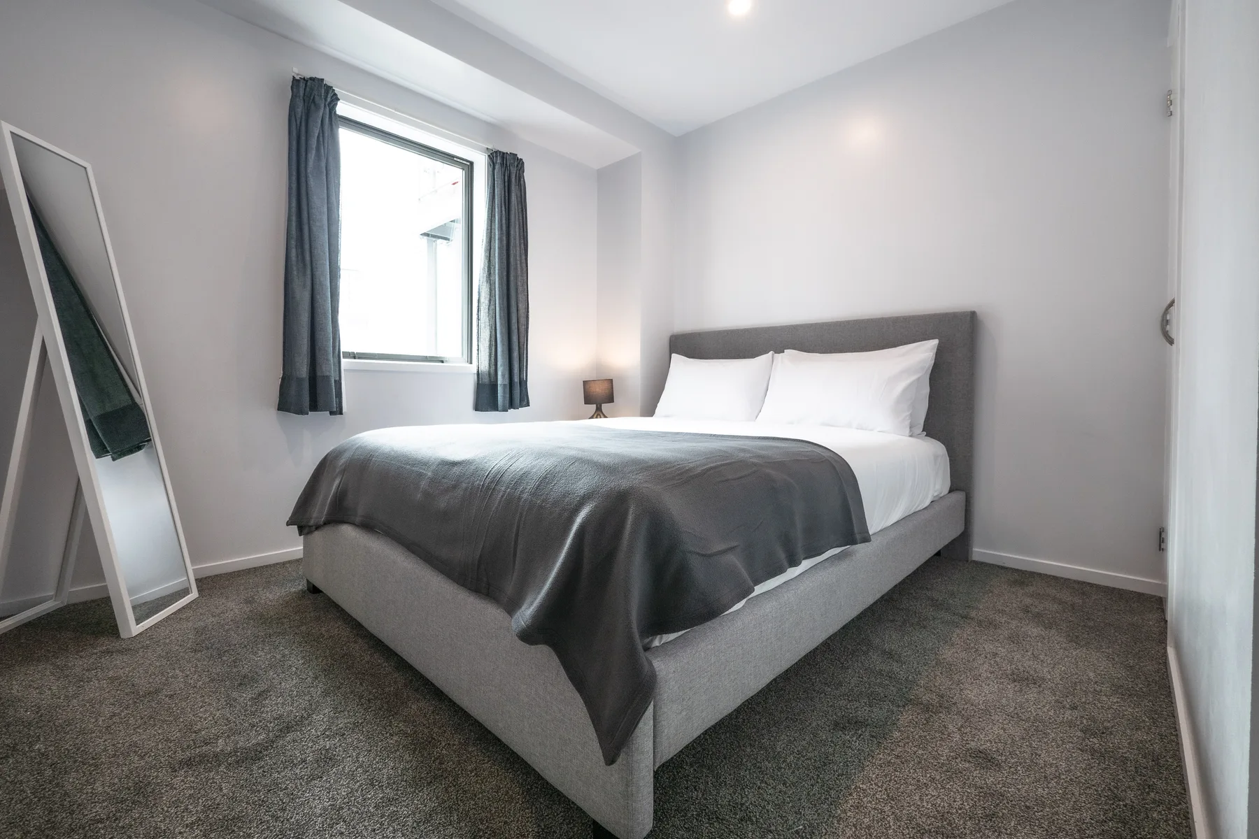 Dormitorio con una cama bien hecha junto a una ventana con cortinas.