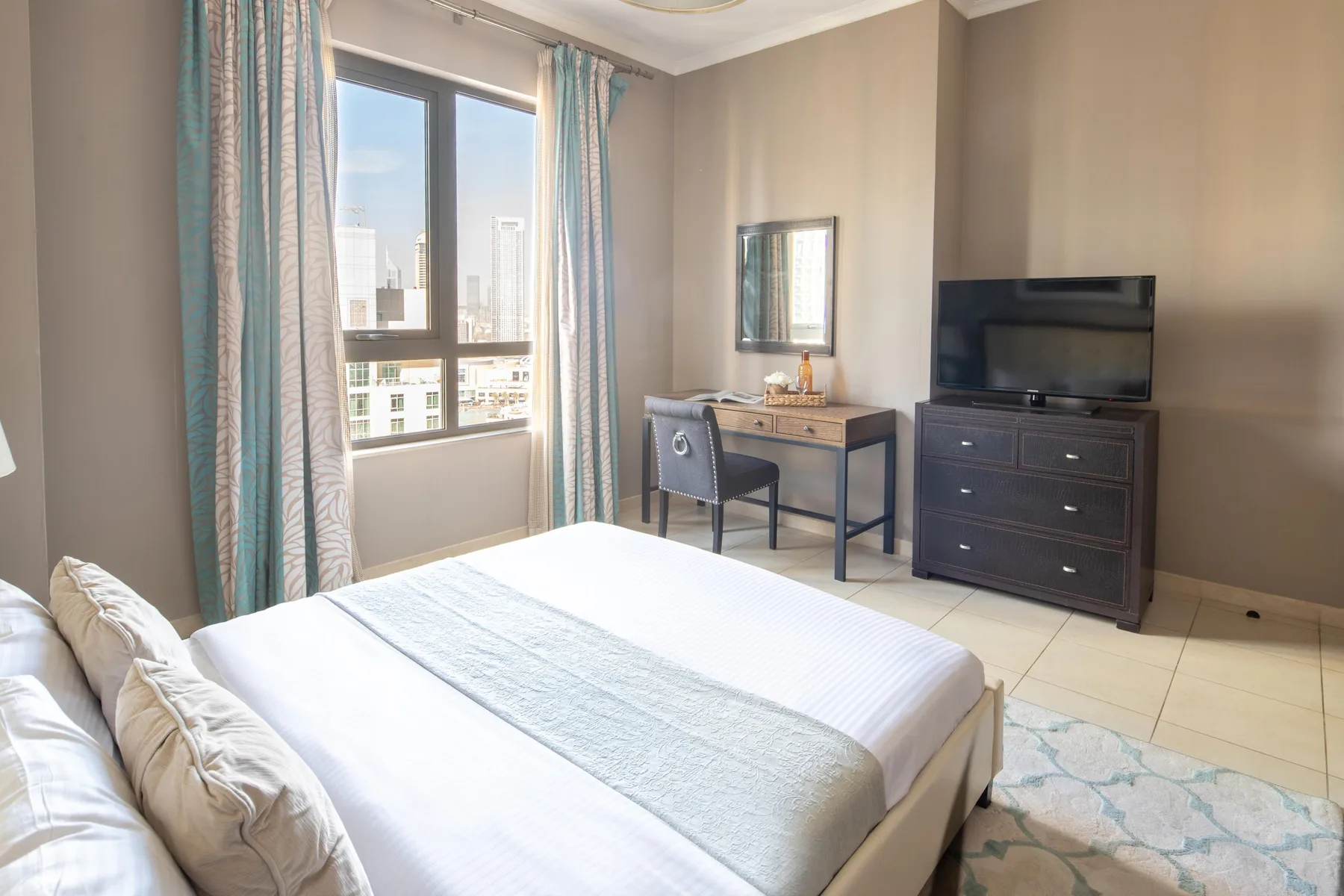 Un dormitorio con una cama, un escritorio y un televisor junto a una ventana grande.