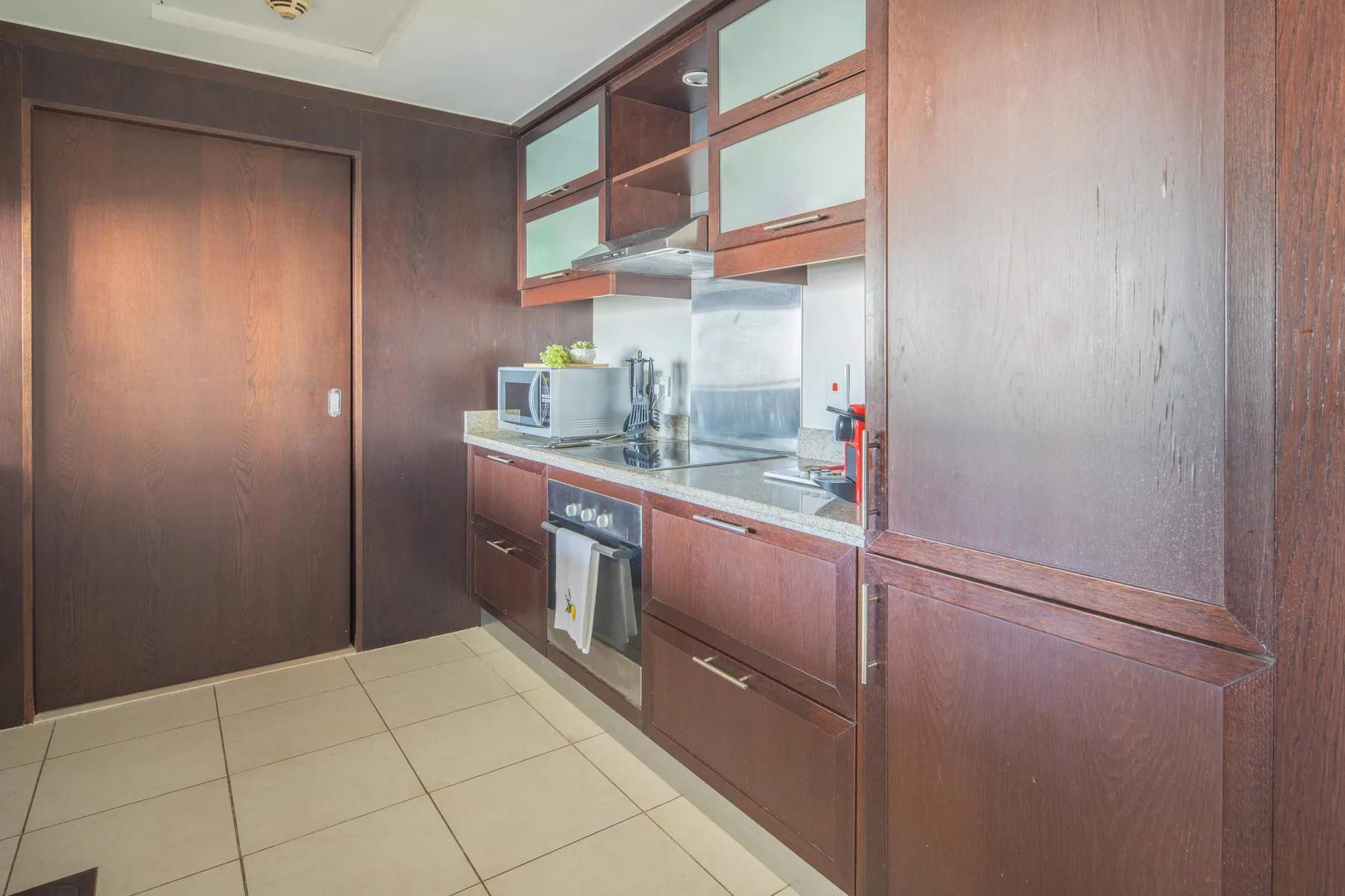 Una cocina compacta con gabinetes oscuros, un microondas y piso de baldosas.