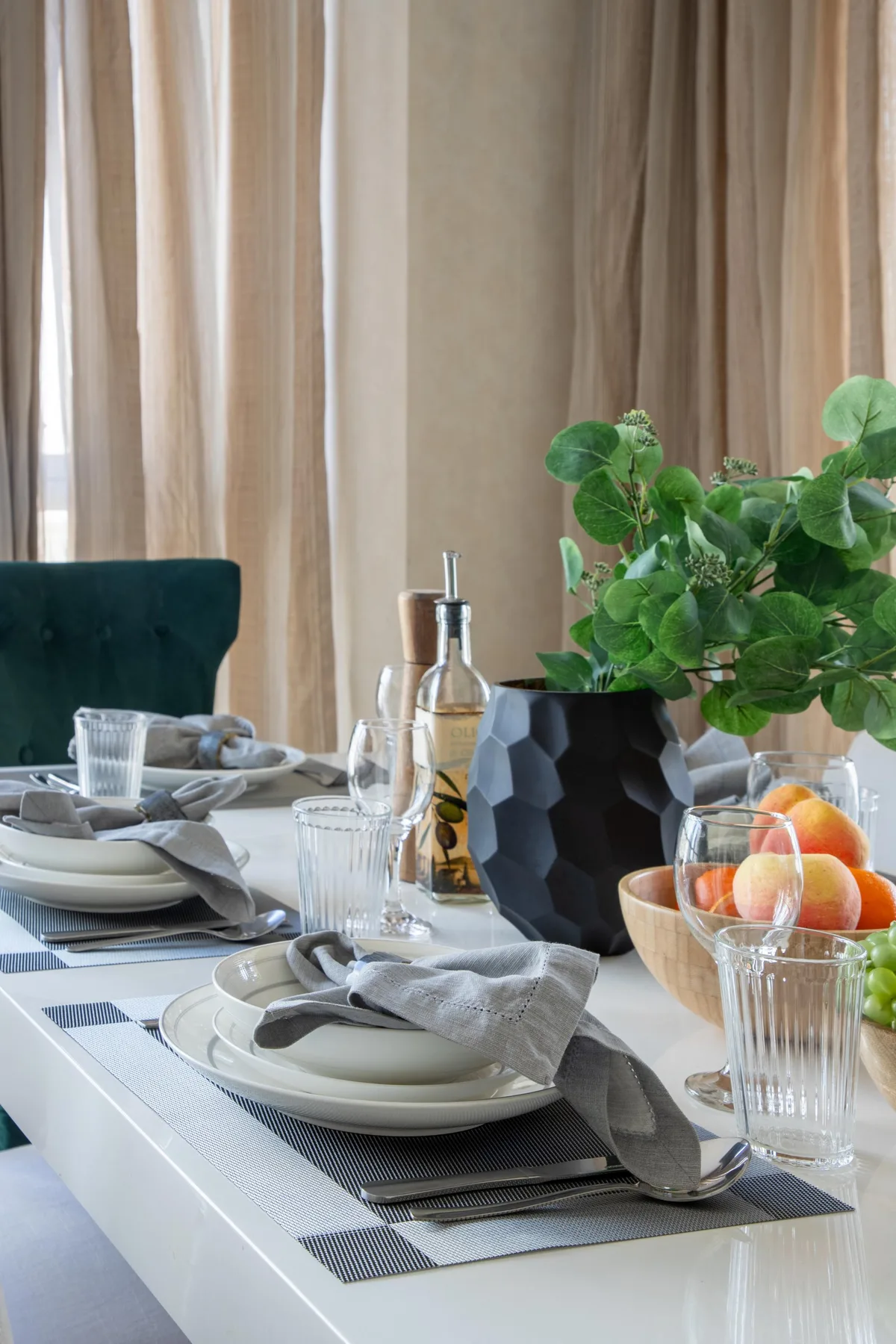 Una mesa de comedor está puesta con platos y vasos junto a una planta frondosa.