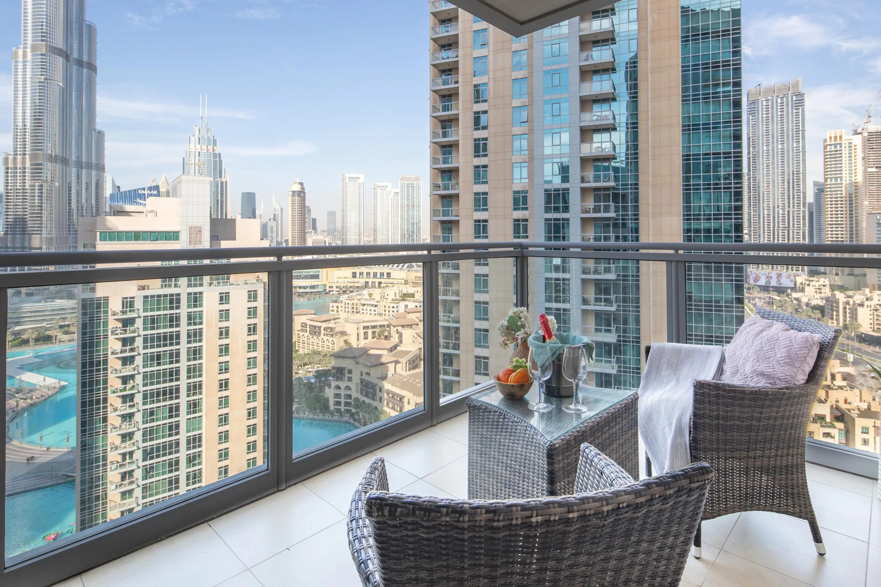 Una zona de estar en un balcón ofrece vistas al perfil urbano, con barandilla de vidrio y una mesa pequeña.